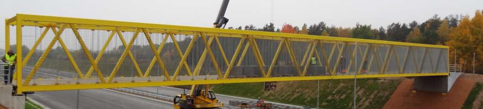 A yellow steel footbridge being installed by crane near Vilnius.